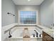 A luxurious soaking tub with a beautiful tile surround is bathed in natural light from a large privacy glass window at 2223 Jon Chris Dr, Harrisburg, NC 28075