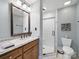 Bathroom featuring granite counters, wood cabinetry, large framed mirror, glass enclosed shower, and modern toilet at 2223 Jon Chris Dr, Harrisburg, NC 28075