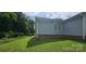 Side exterior featuring light blue siding, brick foundation, green grass, and mature trees under a partly cloudy sky at 2820 Bellhaven Cir, Charlotte, NC 28214