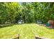 Beautiful backyard featuring a large grassy area, wooden playset, and storage sheds among mature trees at 8938 Glencroft Rd, Mint Hill, NC 28227