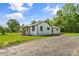 A white house with black trim and a gravel driveway is surrounded by mature trees and a green lawn at 320 E Pine St, Maiden, NC 28650