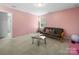 Bonus room with light pink walls, carpeted floors, a futon, and unique coffee table at 10426 Kempsford Dr, Charlotte, NC 28262