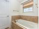 Bathroom with white soaking tub with tiled surround, gold hardware, and neutral colored walls at 12822 Plumleaf Dr, Charlotte, NC 28213