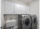 Well-lit laundry room features modern washer and dryer with white cabinets and stainless sink at 4311 Sheffield Park Ave, Charlotte, NC 28211