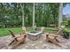 A backyard patio features a stone fire pit with Adirondack chairs, bench seating, and lush green trees and lawn at 12900 Westmoreland Rd, Huntersville, NC 28078
