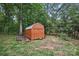 A rustic shed with a wooden door surrounded by mature trees and grassy lawn at 12900 Westmoreland Rd, Huntersville, NC 28078