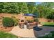 Outdoor stone patio with a fireplace, comfortable seating, umbrella and a retaining wall in a private backyard at 13056 Long Common Pkwy, Huntersville, NC 28078