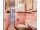 Retro pink tiled bathroom featuring a toilet, sink, cabinet and colorful wallpaper at 611 E Marion St, Shelby, NC 28150