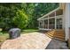 A spacious stone patio extends to a screened porch, overlooking a lush backyard with a barbeque grill at 8441 Sandowne Ln, Huntersville, NC 28078