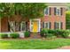 A sunny yellow front door welcomes visitors to this brick home with black shutters and meticulously manicured landscaping at 5517 Alexa Rd, Charlotte, NC 28277