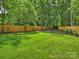 Lush green backyard with a wooden fence, fire pit, and mature trees provides privacy at 112 Manning Dr, Charlotte, NC 28209