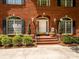 Close-up of the red brick front with arched doorway, trimmed bushes, and decorative sconces at 1209 S South St, Gastonia, NC 28052