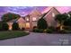 Striking brick home with manicured lawn and circular driveway, illuminated by warm lighting against a vibrant twilight sky at 1509 Churchill Downs Dr, Waxhaw, NC 28173