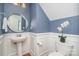Stylish half bathroom featuring blue walls, white wainscoting, pedestal sink, and elegant floral accents at 2548 Chasewater Dr, Indian Land, SC 29707
