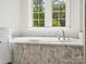 Bright bathroom with a standalone tub and marble patterned tile and a window that lets in lots of natural light at 1008 Ladera Dr, Waxhaw, NC 28173