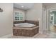 Bathroom featuring a soaking tub with tiled surround under a window and neutral tile floors at 2006 Sandy Pond Ln, Waxhaw, NC 28173