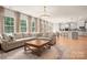 Open-concept living room with a large sofa, hardwood floors, lots of natural light, and a kitchen in the background at 13025 Cinnamon Fern Ln, Charlotte, NC 28227