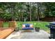 Lush backyard view highlighting the patio with a blue loveseat, flowers, grill, and playground in a wooded area at 16121 Wrights Ferry Rd, Charlotte, NC 28278
