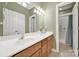 Well-lit bathroom with a double vanity, framed mirror, decorative fixtures, and a tiled shower behind a door at 16714 Hammock Creek Pl, Charlotte, NC 28278