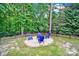 A backyard firepit featuring Adirondack chairs, surrounded by a brick border, black fence, and mature trees at 16714 Hammock Creek Pl, Charlotte, NC 28278