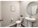 Cozy powder room with a round mirror, pedestal sink, toilet, and minimalist decor creates a serene and inviting space at 700 Windage Way, Pineville, NC 28134