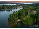 Aerial view of a lakefront property features lush trees, a sandy beach, and a peaceful lake setting under an orange sky at 9184 Greenwood Rd, Terrell, NC 28682