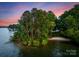 Aerial view of a peninsula features a sandy beach and verdant trees, set against tranquil lake waters under a colorful sky at 9184 Greenwood Rd, Terrell, NC 28682