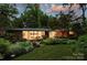 Twilight view of a landscaped home with illuminated interior, highlighting large windows and greenery at 2600 Cloister Dr, Charlotte, NC 28211
