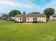 The photo shows the backyard, highlighting the yellow home, a brick chimney, and the spacious, green lawn with a carport at 3537 Heather Ln, Gastonia, NC 28056