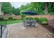 Paver patio with an outdoor dining set under an umbrella, surrounded by lush landscaping at 5917 Bridger Ct, Charlotte, NC 28211