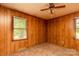 Carpeted bedroom with wood-paneled walls, a ceiling fan, and two windows overlooking the green backyard at 661 Blackwelder Rd, Statesville, NC 28625