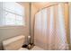 Bathroom with a standard toilet, window and shower/tub with white and red shower curtain at 8698 Rocky River Rd, Harrisburg, NC 28075