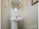 A stylish powder room with a pedestal sink, round mirror, and neutral decor at 7671 Bluff Point Ln, Denver, NC 28037