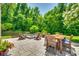 Landscaped backyard oasis with stone patio, outdoor dining, a fire pit with Adirondack chairs, and lush greenery at 7930 Kelburn Ln, Charlotte, NC 28273