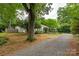 Exterior view of the house nestled amidst mature trees, showcasing the expansive gravel driveway at 34 Admiral Sw Ave, Concord, NC 28027
