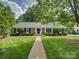 Charming brick home featuring a manicured lawn, mature landscaping, and welcoming walkway to the front door at 6116 Springhouse Ln, Charlotte, NC 28211