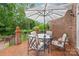 Inviting brick back patio features a glass table with four white cushioned chairs under a large shade umbrella at 7018 Dowington Dr, Charlotte, NC 28277