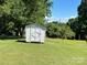 White storage shed in a lush green backyard with mature trees and blue sky at 1412 Beverly Ave, Shelby, NC 28152