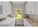 Bright laundry room features white cabinets, appliances, and a window overlooking the landscaped yard at 1500 Lynway Dr, Charlotte, NC 28203