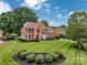 Expansive lawn with manicured landscaping surrounds this traditional brick home with mature trees and blue skies at 15737 Agincourt Dr, Huntersville, NC 28078