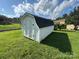 A white storage shed with a gambrel roof sits on a lawn with a fenced yard and other houses nearby at 1735 Hollandale Dr, Gastonia, NC 28054