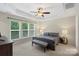 Bright bedroom features tray ceiling, large windows, neutral carpet, ceiling fan, and upholstered bench at 4278 Park South Station Blvd, Charlotte, NC 28210