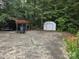 Spacious concrete parking area with a metal carport, shed, mature trees, and flower garden at 9225 Robinson Church Rd, Charlotte, NC 28215