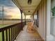 Charming covered front porch with wood floors and comfortable rocking chairs overlooking a tranquil field at sunset at 4115 Jenkins Rd, Marshville, NC 28103