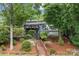 Two story exterior showcasing a deck, large windows, a stone patio, lush landscaping, and lake access at 1111 Palmyra Dr, Fort Mill, SC 29708