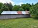 A gray barn with a metal roof is surrounded by lush greenery, showcasing rural charm at 140 Dalu Ln, Harmony, NC 28634