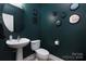 Stylish powder room featuring a modern pedestal sink and dark teal walls, complete with eye-catching mirror accents at 6914 Evanton Loch Rd, Charlotte, NC 28278