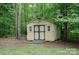 Exterior of a small, light-colored outbuilding nestled among mature trees, offering potential for storage at 1565 Earnhardt Rd, Salisbury, NC 28146
