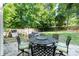 Landscaped backyard with a stone patio featuring an outdoor table set, grill, and mature shade trees at 2206 Waters Trail Dr, Charlotte, NC 28216