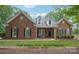 Charming brick home featuring dormer windows, black shutters, mature landscaping, and a welcoming front porch at 105 Prairie Rose Ct, Waxhaw, NC 28173